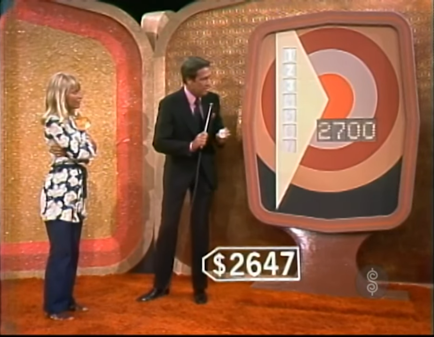 Bob Barker stands beside the Bullseye 1972 pricing game board, while a contestant watches. The board displays a target with a price of 00 and a marker indicating the contestant's current guess of 47.