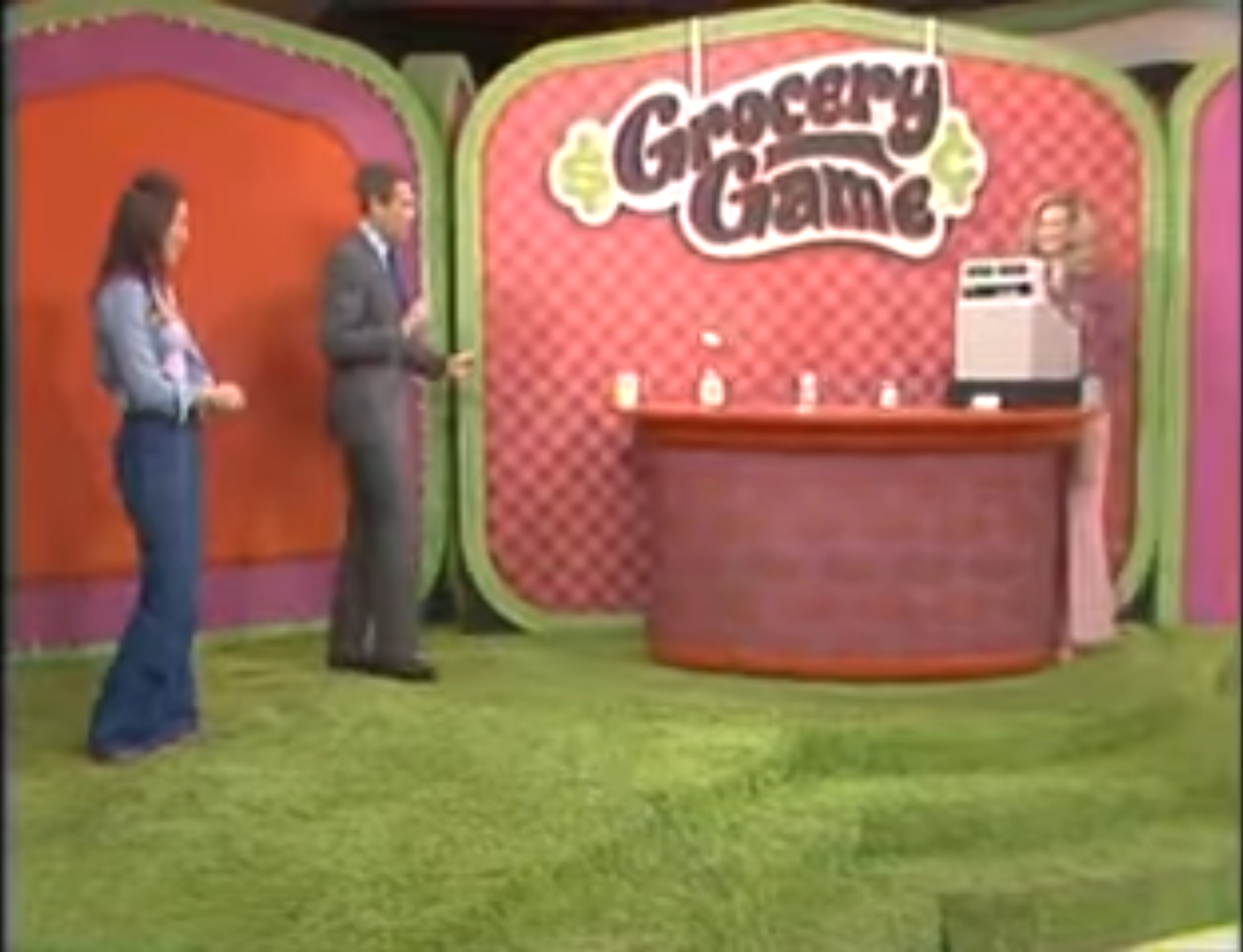 Contestants participate in the Grocery Game on The Price is Right with an old-fashioned cash register in a colorful set designed for the game.