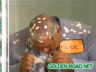 Contestant Lee is surrounded by confetti inside a shower stall on The Price is Right, wiping his glasses after making a selection.