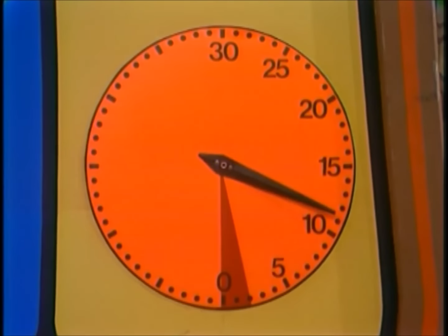 A close-up of an orange clock face with black markings, showing the second hand pointing just past the 10-second mark.