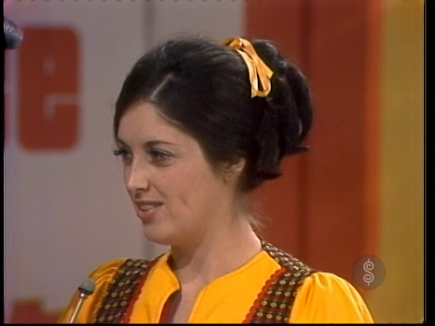 A contestant smiles while participating in the 'Five Price Tags' game on The Price is Right, wearing a yellow outfit with a patterned vest.