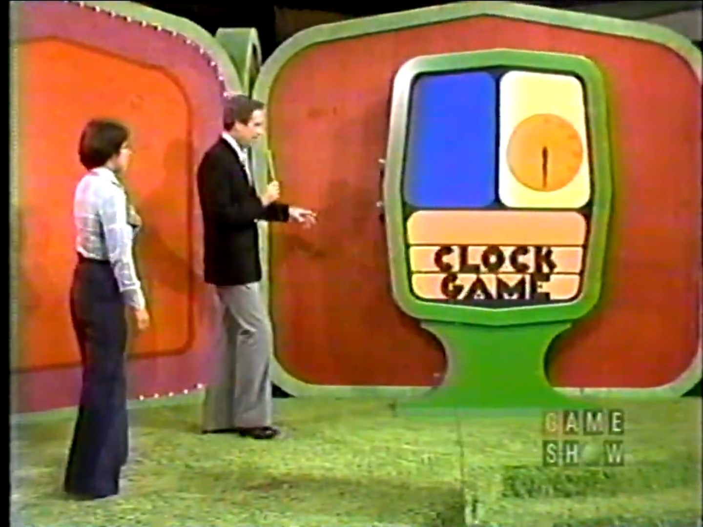 Contestant and host in front of the Clock Game display on a game show set.