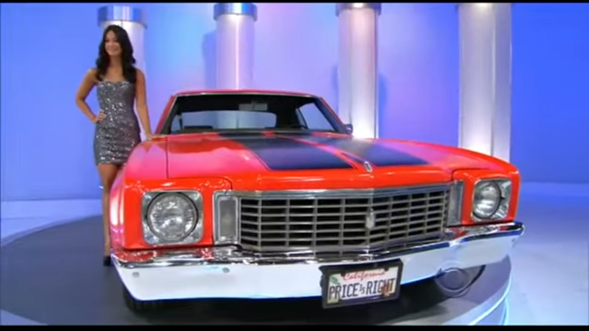 A model stands next to a classic red car with a black stripe,