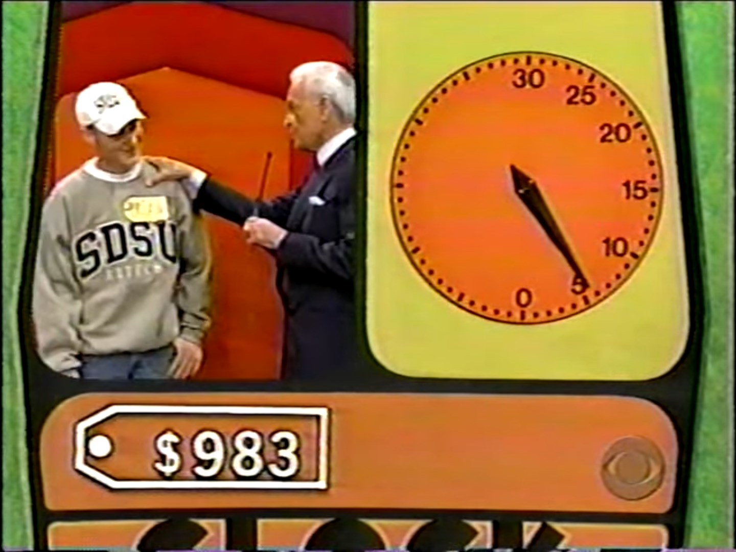 Contestant smiling next to Bob Barker with a stopwatch displaying time, competing in the Clock Game, showcasing a prize tag of 3.