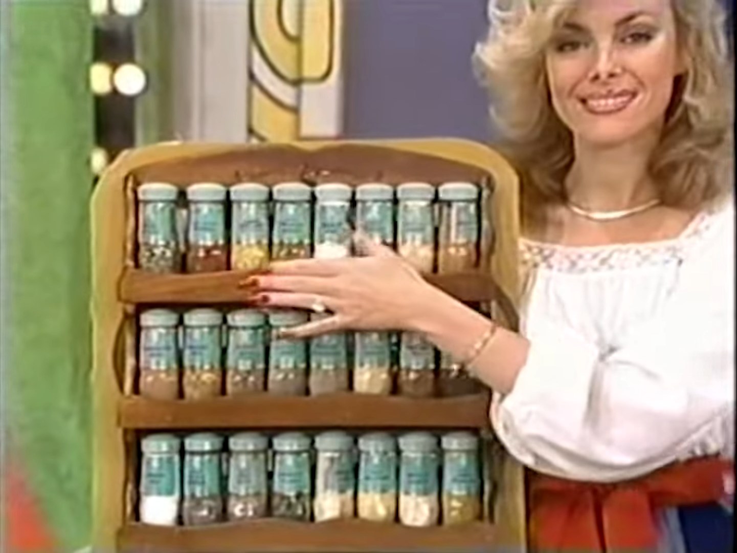 A woman presents a spice rack filled with glass jars containing various spices on a game show set.