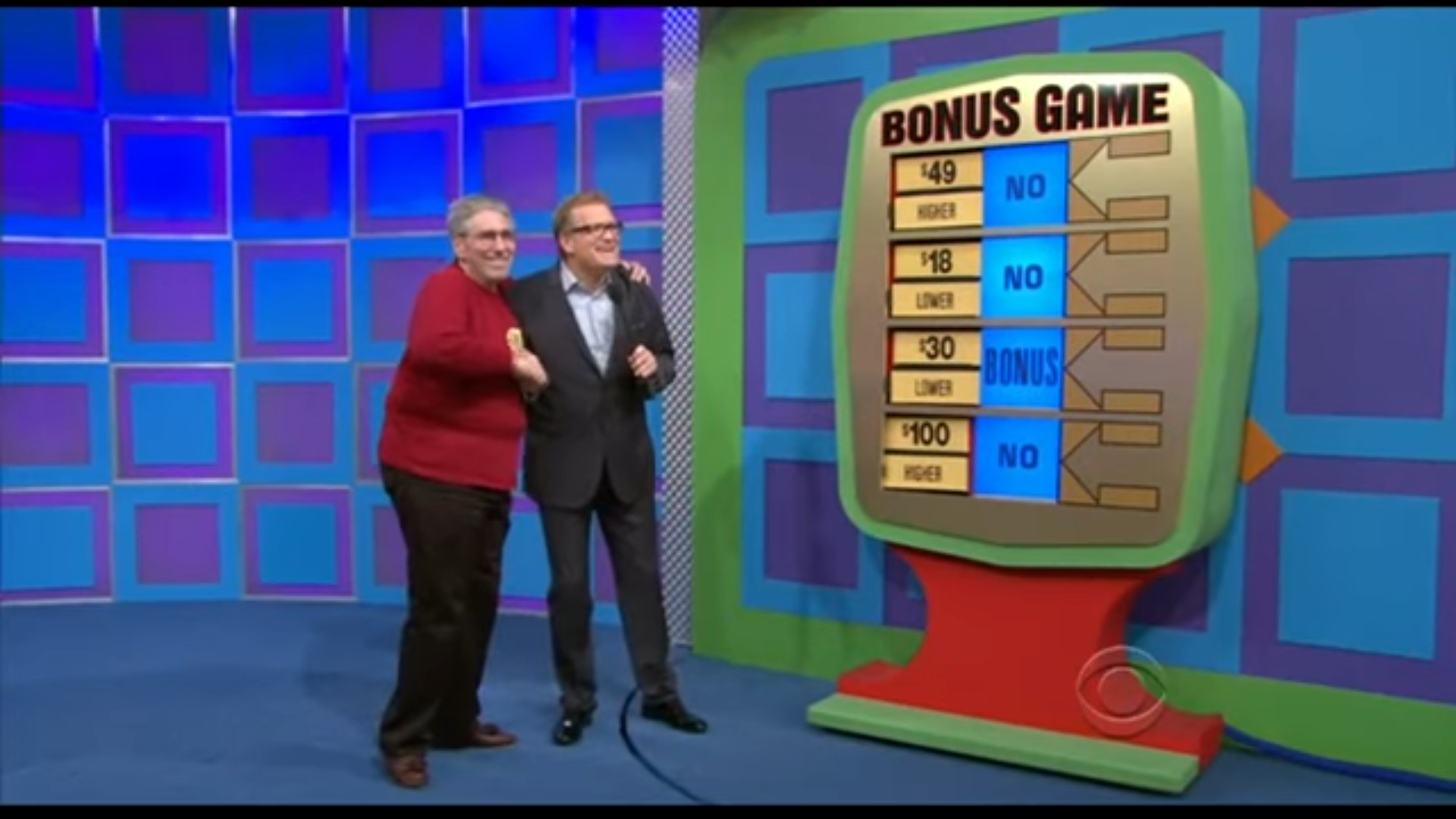 Paul and Drew Carey pose together in front of the Bonus Game board, smiling as they celebrate a win, with various prize amounts displayed.