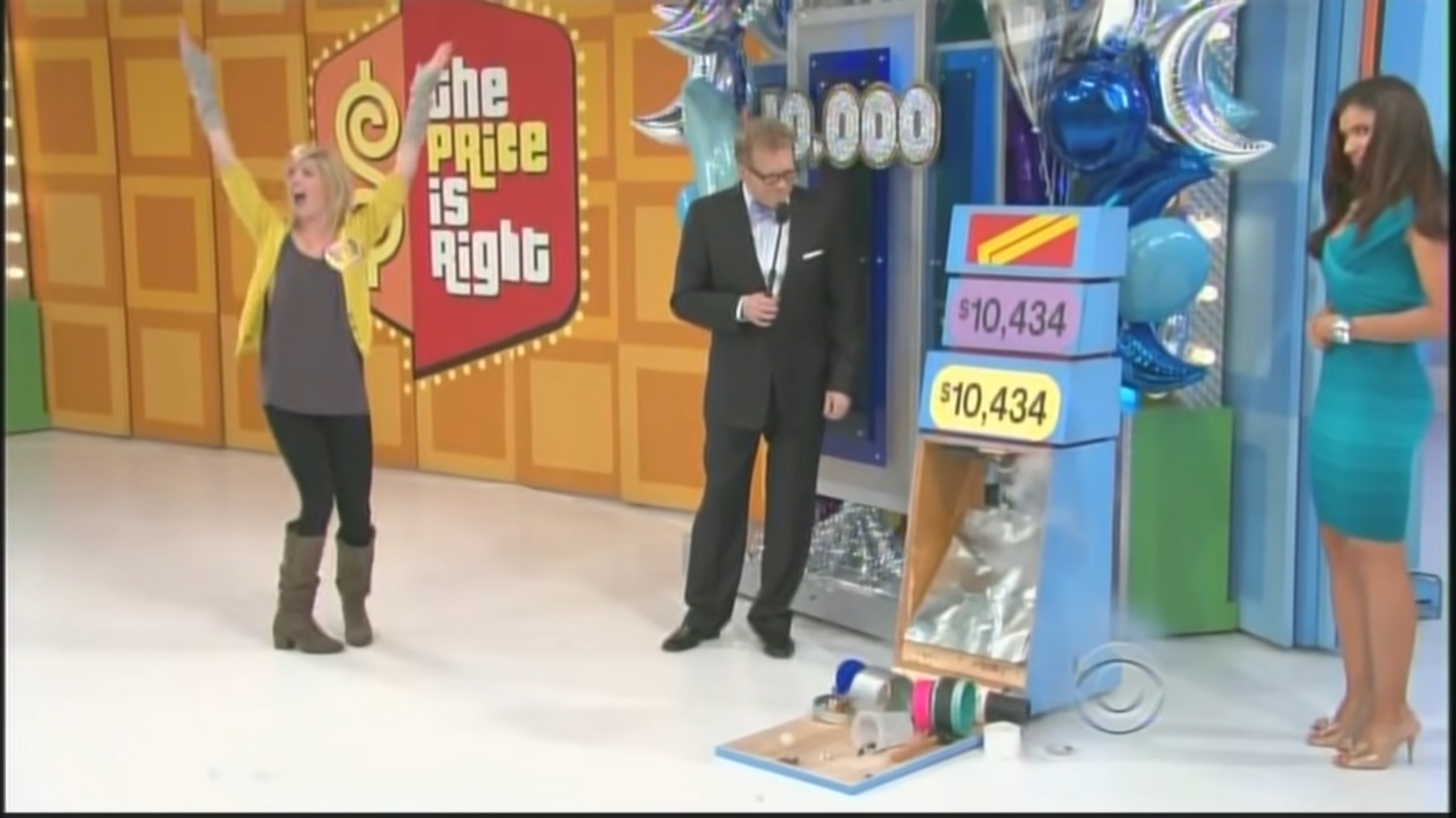 A contestant celebrating with raised arms while Drew Carey presents a pricing board showing two price tags, both indicating ,434, on the set of The Price is Right.