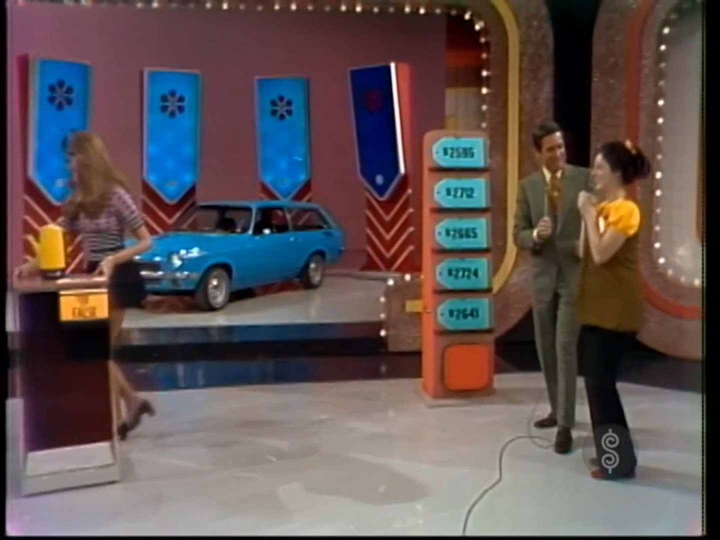 A contestant celebrates while Bob Barker stands nearby, with a blue car displayed in the background alongside price tags on The Price is Right.