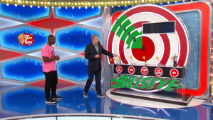 Drew Carey gestures towards a colorful game board labeled 'BULLSEYE' while a contestant stands beside him, both appearing on the set of The Price is Right.