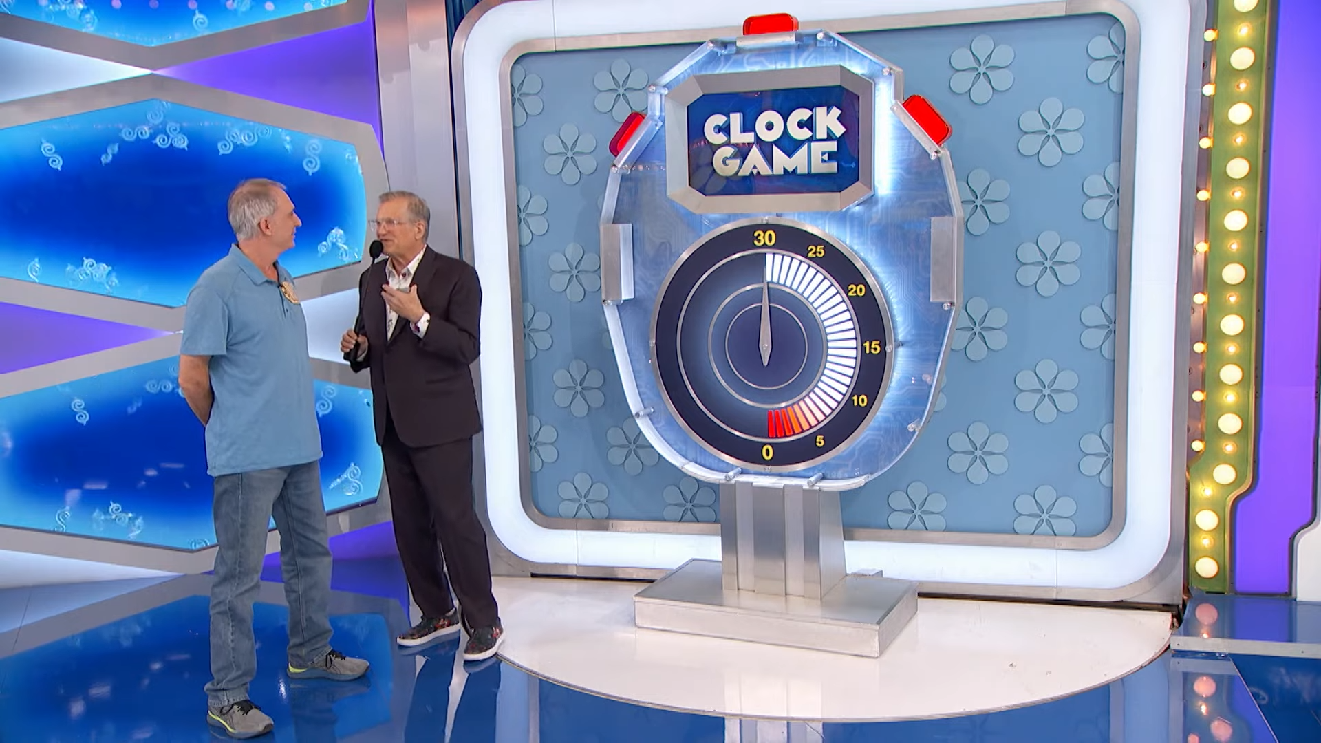 A contestant and Drew Carey engage in the Clock Game, featuring a large timer and a vibrant game show backdrop.