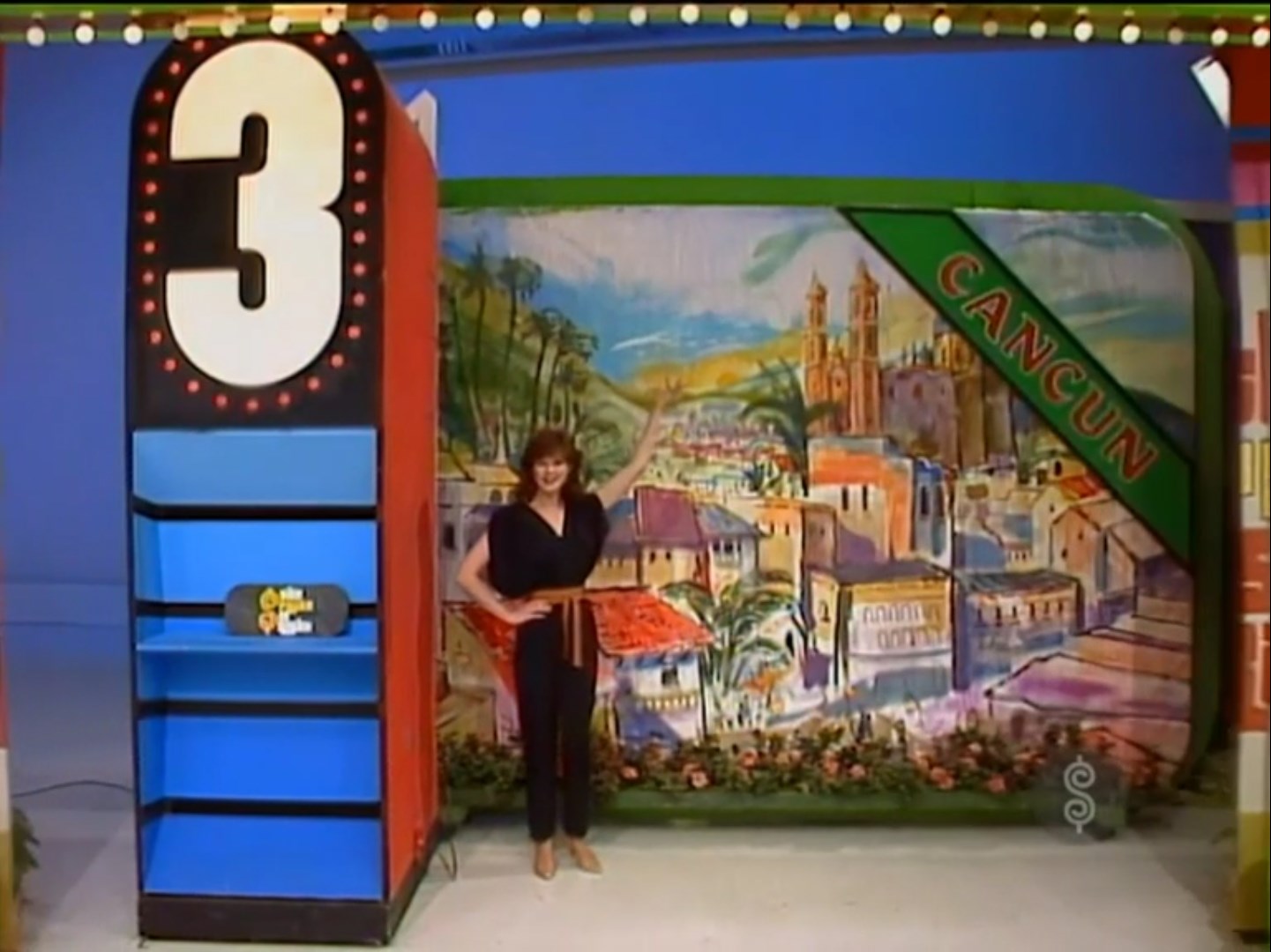 A model stands next to prize number 3 in the game 'Most Expensive' on The Price is Right, with a backdrop featuring a vibrant illustration of Cancun.