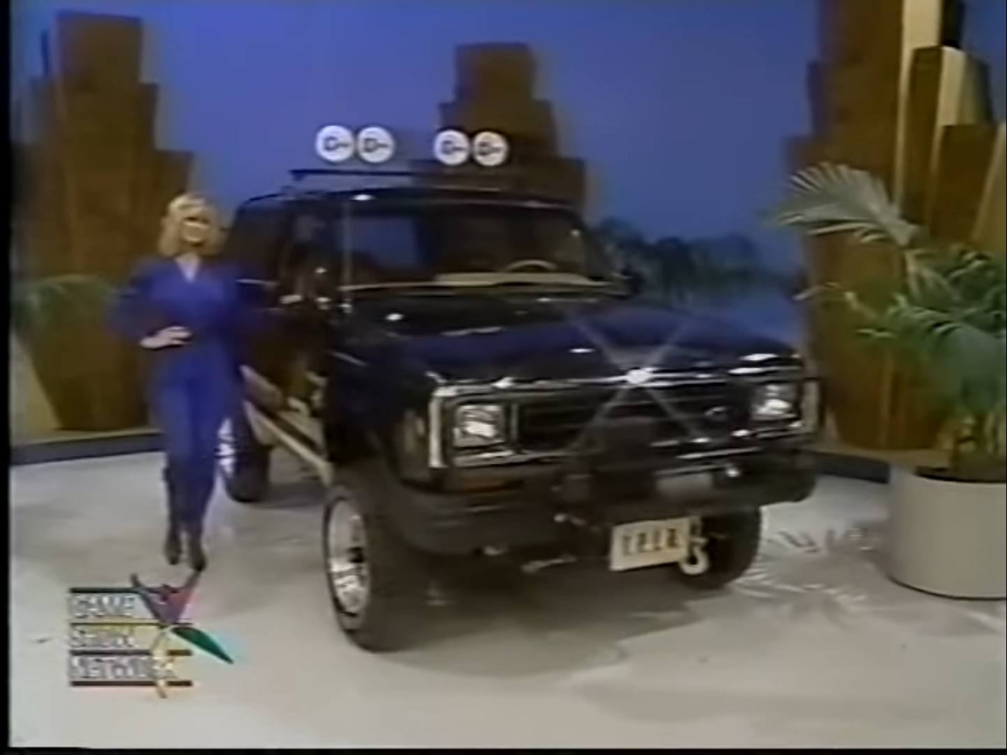 A model poses next to a black Ford Bronco II SUV with decorative lights on top, showcasing a set for a game show.