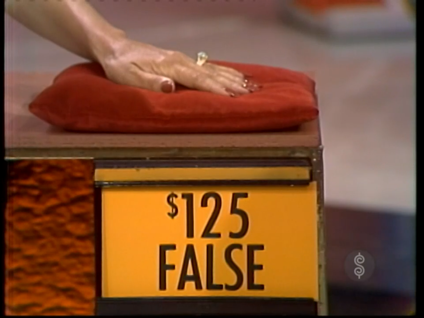 A contestant's hand rests on a red cushion while indicating that the price of 5 is false.