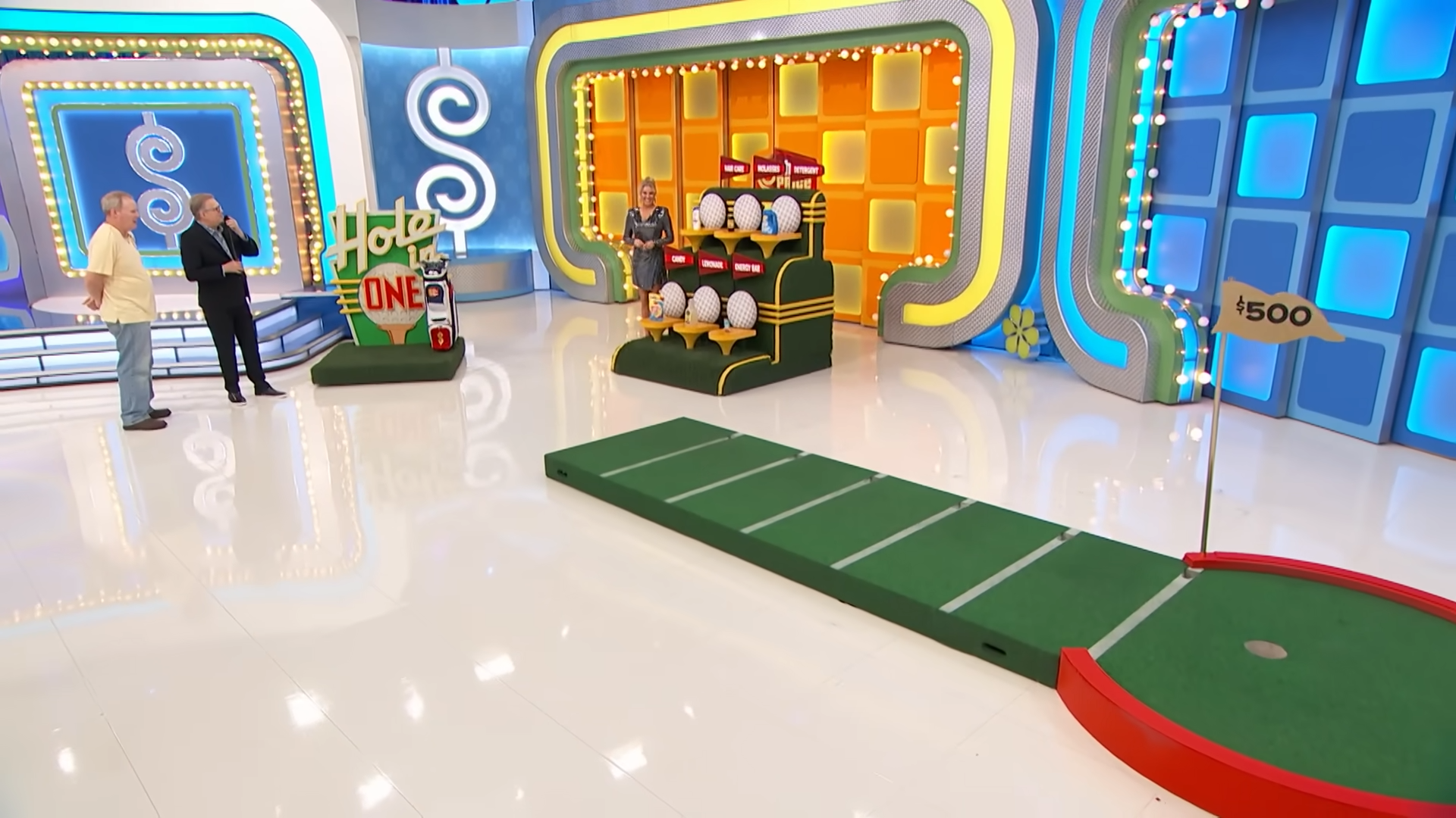 Scene from the game show The Price is Right featuring the 'Hole in One' game setup with a putting green, a contestant, and the host discussing the gameplay.