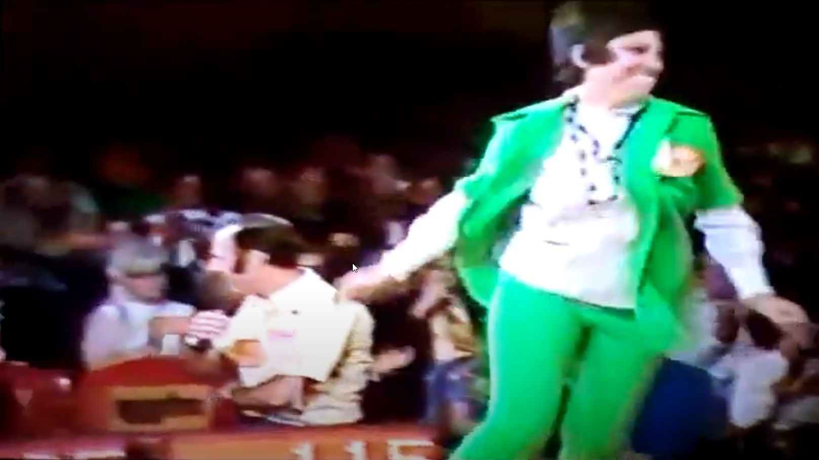 A contestant in a green outfit walks onstage on The Price is Right with enthusiasm, while a host speaks to the audience, surrounded by cheering fans.