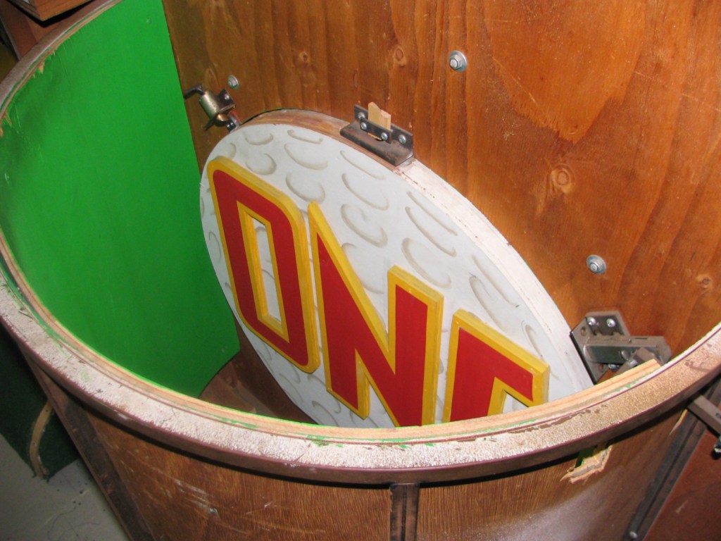 Close-up view of a circular sign with the word 'ONE' in bold red letters, positioned within a wooden structure with a green interior.