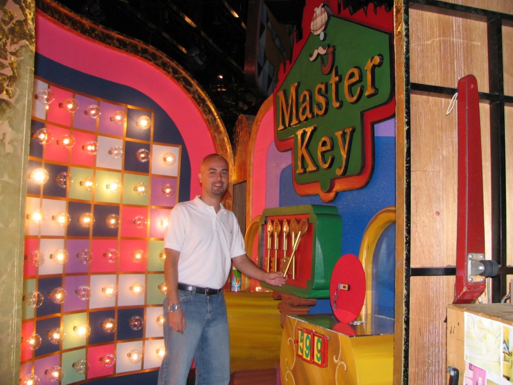 A person standing next to the colorful 'Master Key' game set, featuring a bright backdrop with various lights.