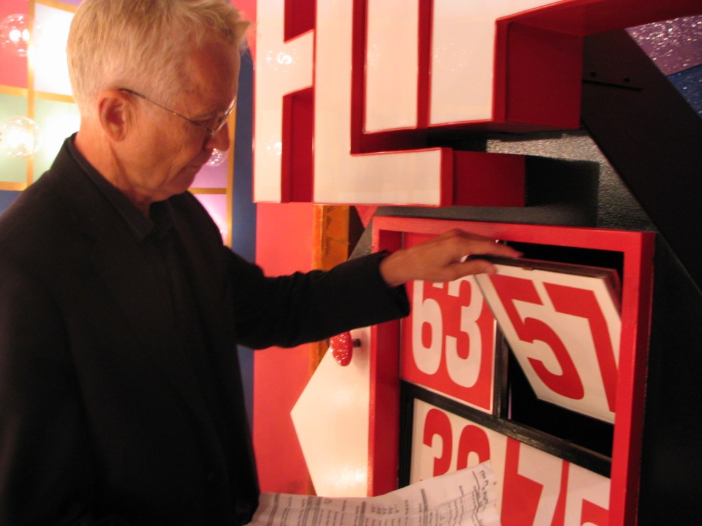 Roger Dobkowitz examines a slot with red and white numbers and a sheet of paper while backstage during a television taping.