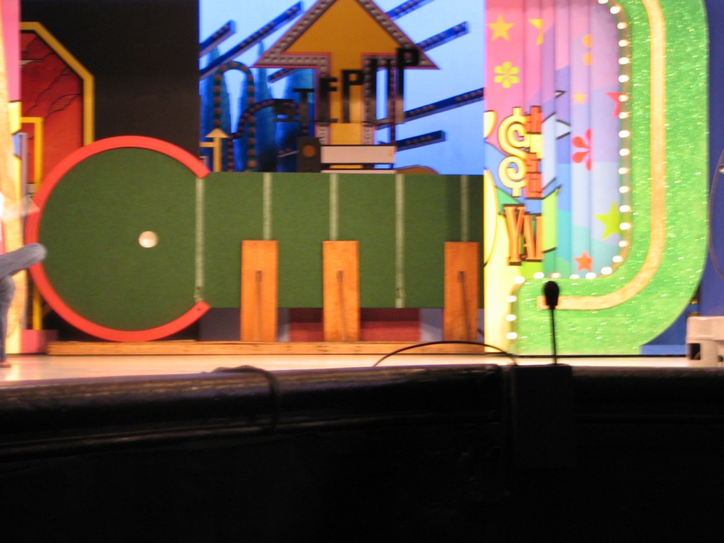 A colorful stage set from The Price Is Right, featuring various game elements and props, with a microphone in the foreground.