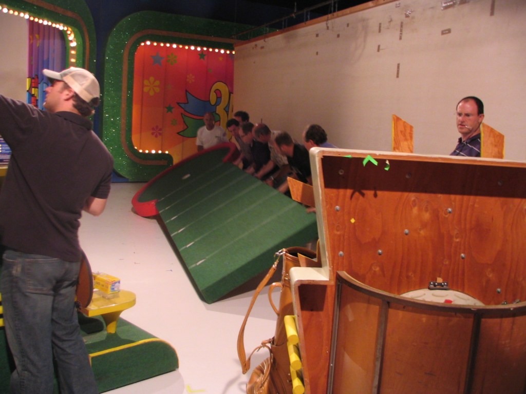 Behind-the-scenes photo from the taping of 'The Price is Right', showing crew members moving a large set piece on stage.