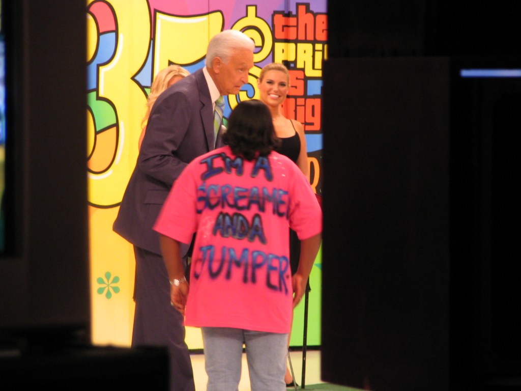 A contestant wearing a bright pink shirt that reads 'I'm a screamer and a jumper' interacts with a host on stage, with a colorful backdrop representing the 35th season of a game show.