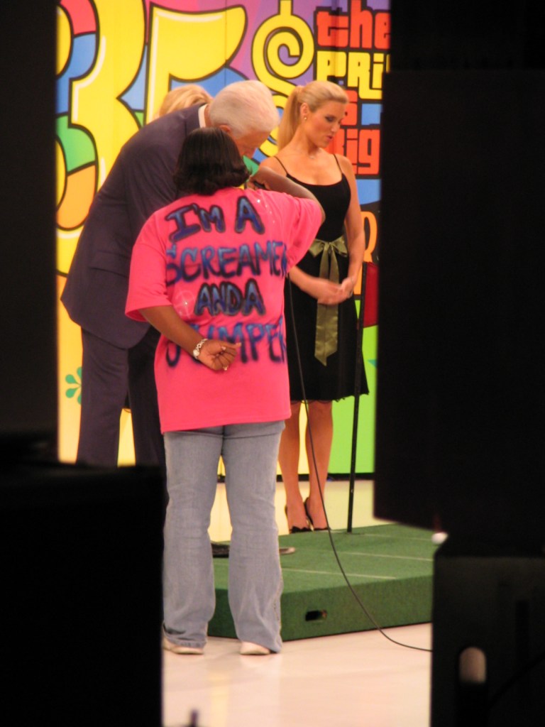 A contestant in a pink shirt reading 'I'm a SCREAMER AND A JUMPER' interacts with the host and model on set during the 35th season premiere of The Price Is Right.