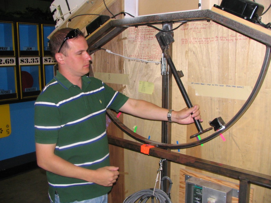 A person adjusting equipment backstage at a game show set, with colorful game pieces and panel displays in the background.