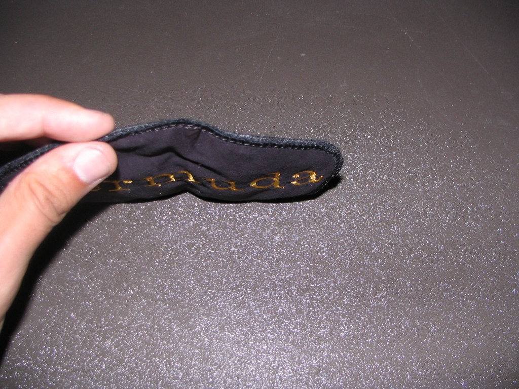 A hand holding a black fabric item with gold lettering that appears to read 'Bermuda,' set against a textured dark surface.