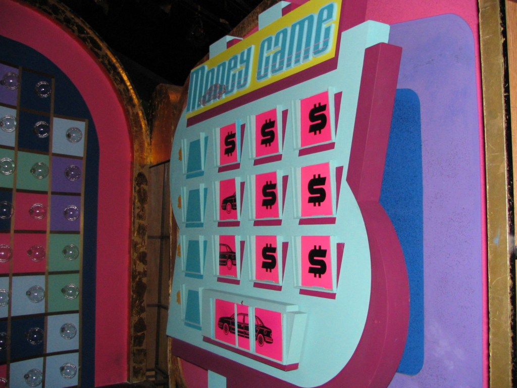 Colorful game board featuring the '$' symbol and images of cars, set against a vibrant pink and blue background, reminiscent of a classic game show.