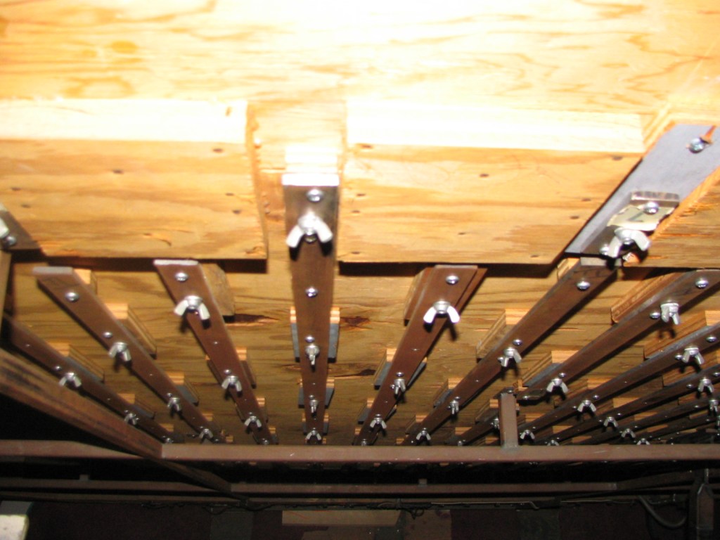 Close-up view of backstage support structure featuring wooden planks secured by metal brackets and rods, showing the intricate setup used for production.