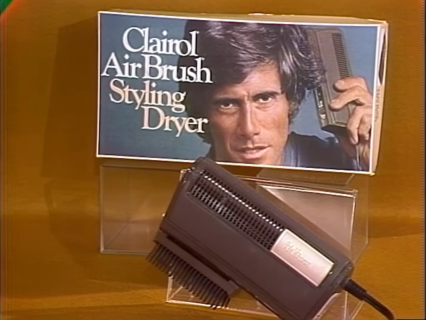 A Clairol Air Brush Styling Dryer displayed on a stand with a box featuring a model using the product in the background.