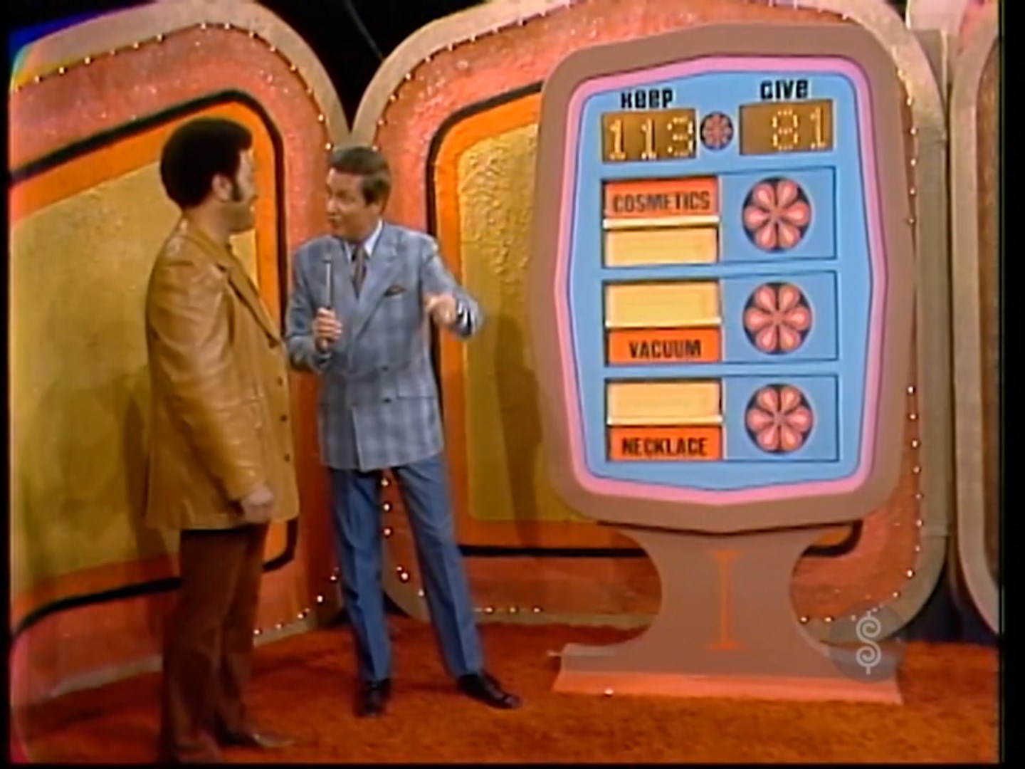 Contestants stand in front of the Give or Keep game board on The Price is Right, displaying scores for 'KEEP' (113) and 'GIVE' (81) with items listed: cosmetics, vacuum, and necklace.