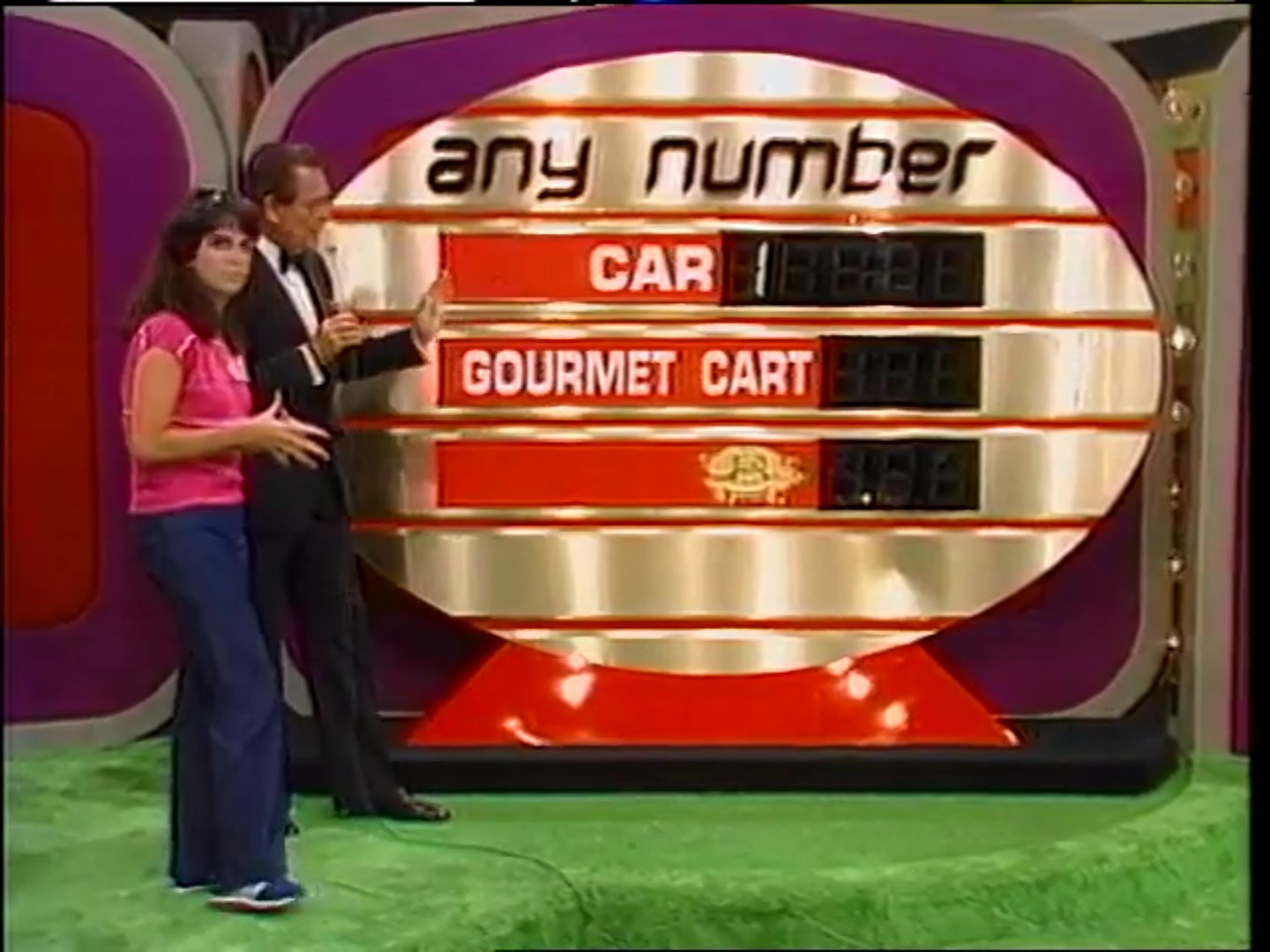 Contestant and host standing beside the 'Any Number' game board displaying a car and gourmet cart prizes with associated prices.