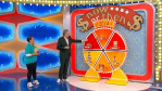 Drew Carey demonstrates the 'Now or Then' pricing game on The Price is Right, featuring a large wheel divided into sections with colorful graphics and game pieces, while a contestant in a blue shirt watches.
