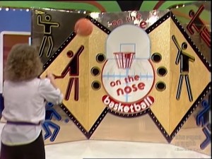 Contestant playing the basketball pricing game "On the Nose" on The Price is Right, featuring colorful background graphics and a hoop.