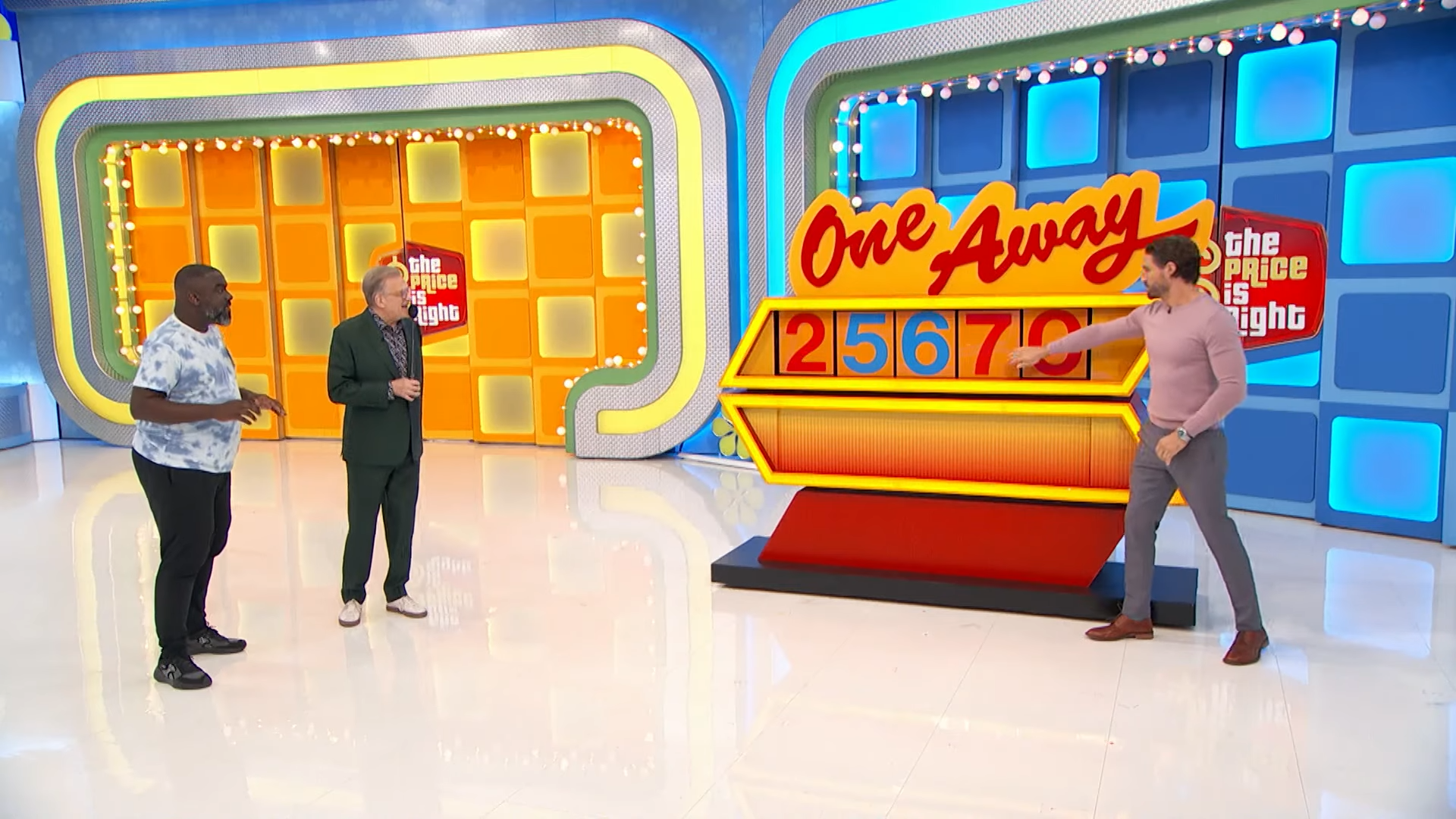 Contestants and host interacting with the One Away pricing game display, featuring the numbers 25670.