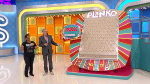 A contestant and host standing next to the Plinko board on The Price is Right set, featuring colorful backgrounds and lights.