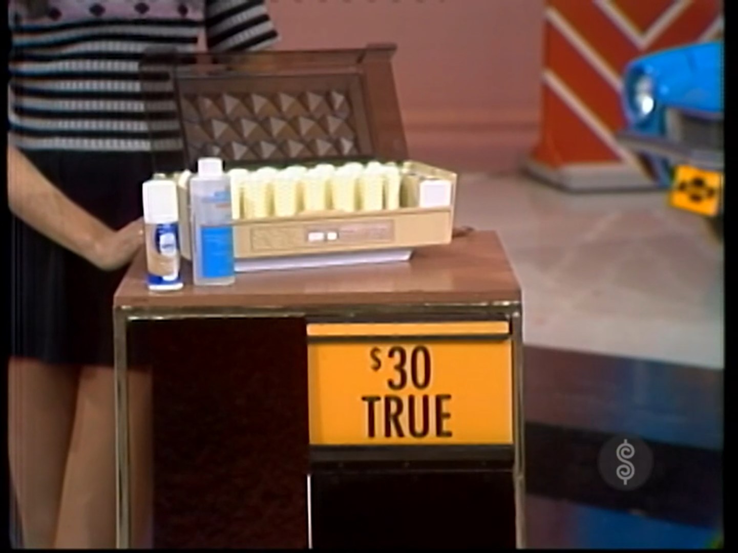 A game segment from 'The Price is Right' showing a price tag labeled ' TRUE' next to a hairstyle setter and beauty products.
