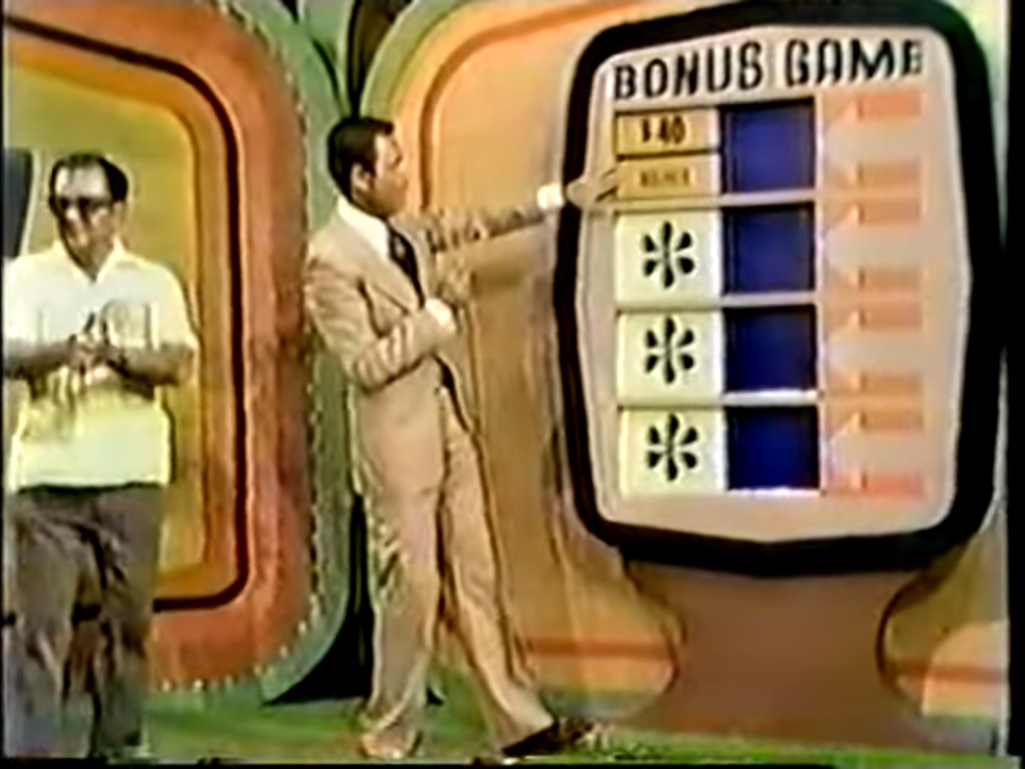 A game show host explains the Bonus Game while a contestant looks on, with a colorful game board featuring three prize windows and a score indicator.
