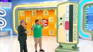Contestant playing the 'Range Game' on The Price is Right, with a host guiding him and a game board in the background.