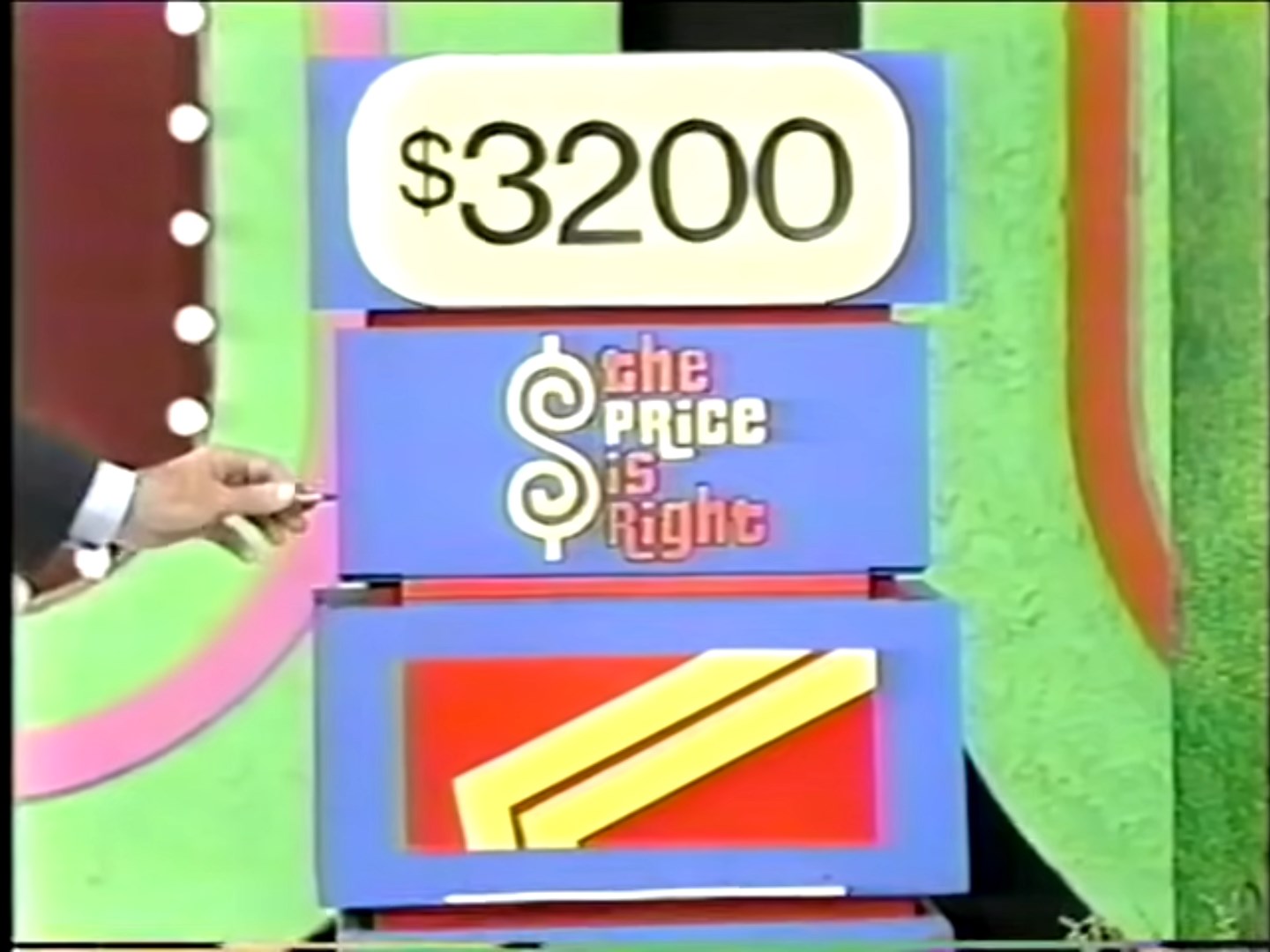 A colorful game show set featuring a price display reading '00' with the words 'The Price is Right' below it, and a hand holding a pen pointing at the display.