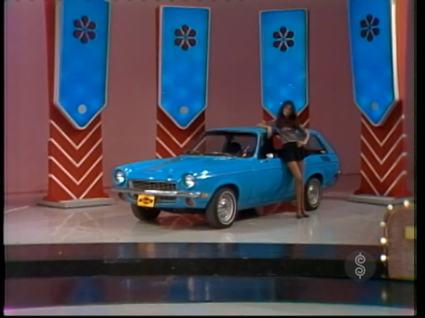 A blue 1972 Vega Kammback Wagon on a game show set, with a model posing beside it.