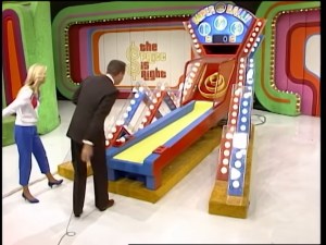 Bob Barker and a contestant interact with the Super Ball game on The Price is Right set, showcasing a colorful red and blue Skee Ball ramp.