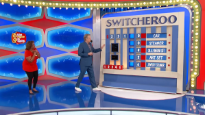 Drew Carey introduces the 'Switcheroo' pricing game on The Price is Right, with a contestant standing beside him. The game board displays numbers and options in a colorful setting.