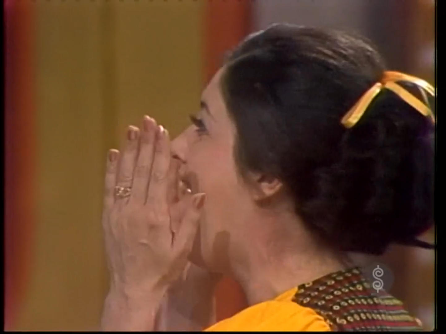 A contestant expressing excitement with her hands over her mouth while wearing colorful attire during a game show.