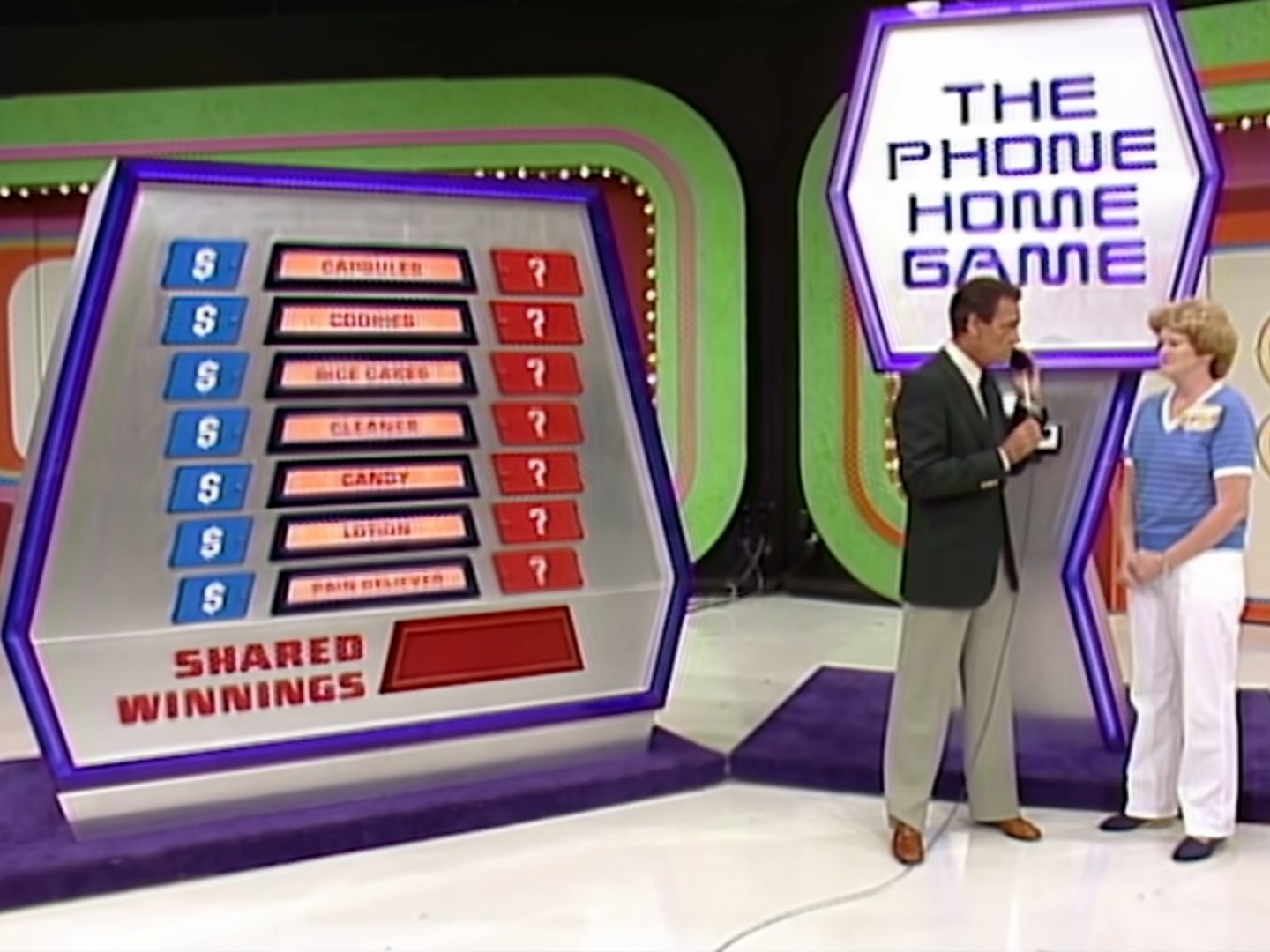 The Phone Home Game on The Price is Right displays a game board displaying grocery items and their associated prices as Bob Barker interacts with a female contestant.