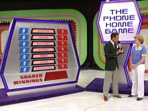 Bob Barker and a contestant stand beside a colorful game board displaying options and categories for 'The Phone Home Game' on The Price is Right, with visible shared winnings.