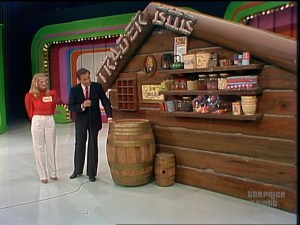 The 'Trader Bob' set featuring a wooden stand with shelves displaying various items, a barrel, and Bob Barker speaking with a female contestant.