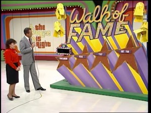 A scene from The Price is Right featuring Bob Barker speaking beside a female contestant in front of the 'Walk of Fame' game display with colorful stars and prizes including a car, trip, and hot tub.