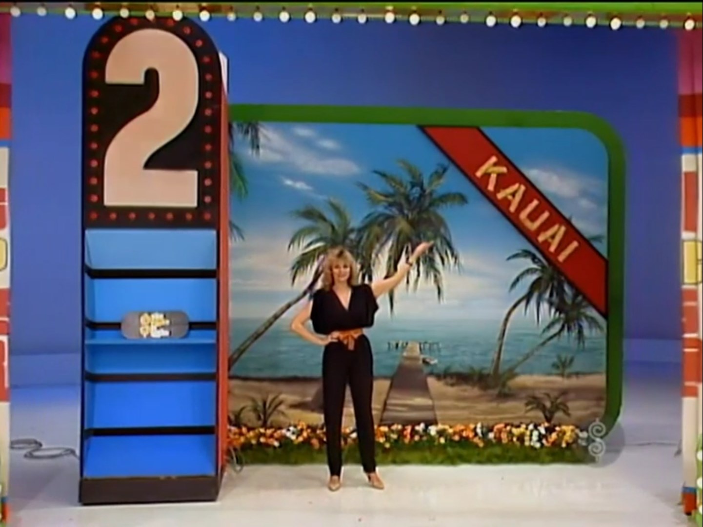 A model showcases the prize number '2' for a trip to Kauai, standing in front of a tropical backdrop with palm trees and a beach.